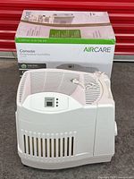 Front and side view of AirCare evaporative humidifier with original box in background showing product name and branding.
