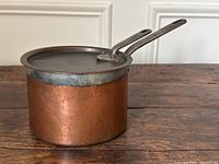 Full view of copper saucepan with iron lid on, showing hammered texture and patina.