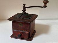 Front and side angled view of antique wooden coffee grinder with metal grinding lid and handle, showing overall shape and handle rotation