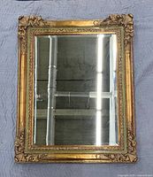Full front view of the gilt wood-framed mirror laid flat on moving blanket