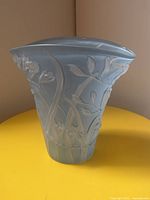 Front view of blue frosted glass fan vase with raised floral freesia design on a yellow surface.
