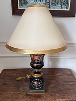 Full view of the urn style wooden lamp with cream shade and floral painted base on wooden table.