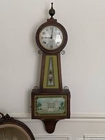 Full view of the banjo clock hanging on wall.