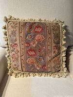 Front view of the needlepoint decorative pillow showing floral design and fringe.