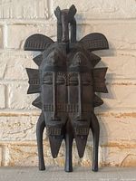 Full front view of carved mask against white brick