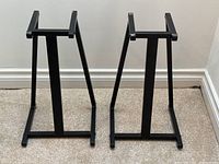 Pair of black metal speaker stands side by side on carpeted floor.