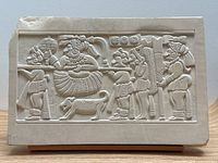 Front view of the rectangular carved stone panel showing five ancient Mexican figures and a dog, with a chip on the bottom left corner. Mounted on wooden stand.