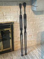 Full view of the two tall, dark wooden tribal figures leaning against a white brick wall next to a fireplace.