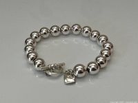 Silver plated beaded bracelet laid out on a white surface, showing round beads and toggle clasp with logo charm.