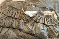 Two sets of two muted sage green silk curtains with gathered tops and sewn-in hooks, laid flat showing the front and back sides with white blackout lining visible.