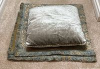 Pillow and folded blanket on carpet, showing velvet fabric texture and fringe edge details on blanket.