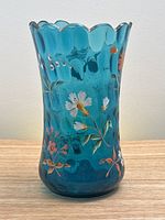 Front view of blue glass vase showing hand painted floral details and scalloped top rim