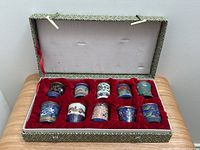 Full display of the original box containing 10 cloisonné jars with red velvet lining, showing two rows of miniature jars.