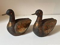 Pair of carved wood duck figurines showing side view, brass and copper armor on wings and chest, dark wood with brass beaks.