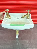 Front view of porcelain sink with brass faucets mounted, green tape note visible