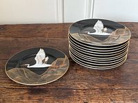 Stacked plates with one plate separate, showing full set of 12 with crane design and gold wave pattern on black background