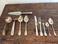 Assortment of serving and table pieces laid out on wooden surface: carving knife, soup ladle, serving fork, serving spoons, plus several table utensils