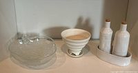 Photo showing all three items: glass lidded bowl, ceramic strainer bowl and stand, and white ceramic oil and vinegar set with two corked bottles in tray.