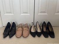 Full view of four pairs of women's shoes - black leather pumps with buckles, nude loafers, black slingback heels, black block heels.