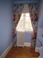 Blue floral curtains hanging in window with natural light showing full length and floral pattern draping over radiator.