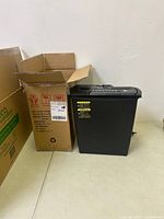 Amazon Basics paper shredder beside its original box on a light floor against a white wall.