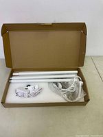 Open cardboard box showing three white fluorescent tubes, power cord, timer module, and adapters wrapped in bubble wrap.