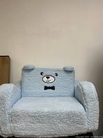 Front view of kids blue plush teddy bear pull-out couch showing teddy bear face with ears and black bow tie on backrest.