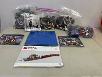 Full view of multiple bags of LEGO pieces, instruction books for Harry Potter LEGO sets, and blue base plate on table.