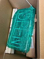 Box containing a green transparent LED light fixture wrapped in plastic and several white boxes.