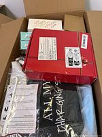 Open cardboard box showing a red box, packaged men's and women's socks, and other small packaged items