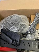 Top-down view inside box showing smartphone case, black power strip, and braided cable.