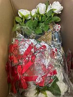 Photo of box containing artificial white roses and red ribbon decorations in plastic wrapping.