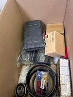 Box containing mixed miscellaneous items including electrical components, hardware parts, belts, and packaged night light.