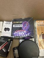 Top view of box showing LED strip light, USB dual adapter, car aromatherapy device, digital scale, and cat scratching mat.