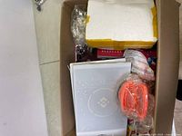 Top view of large box showing white binder, orange plastic item, foam piece, and various other items inside box.