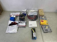 Various automotive small parts including spark plugs, ignition wires, seals, and wiring in packaging arranged on a flat surface.