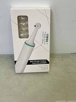 Front view of the multifunctional tooth cleaner device in its original packaging, showing the product and four replacement heads.