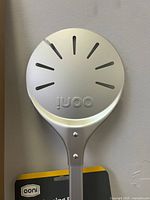 Top view of the round pizza peel paddle showing the brand name 'ooni' with multiple slots.