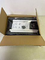 Two black sliding drawers packed in box with metal rails, assembly instructions, and mounting hardware visible.