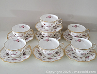 Seven bone china teacups paired with matching scalloped saucers arranged in two rows