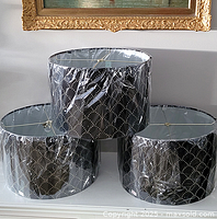Three brand new black lamp shades with silver stud pattern stacked, wrapped in protective plastic.