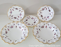 Two scalloped-rim soup bowls and three matching plates arranged in group shot
