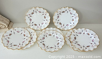 Six plates arranged in two rows showing scalloped edges, floral pattern and gold trim