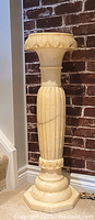 Full front view of alabaster pedestal stand against brick wall