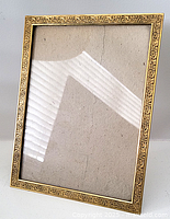 Front view of antique brass easel frame with glass cover showing ornate embossed floral and scrollwork design and wear marks.