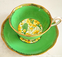 Top-down view of teacup and saucer showcasing green exterior and yellow floral pattern inside the cup and on the saucer center with gold trim.