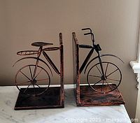 Pair of metal bicycle shaped bookends shown from front angle on marble surface with neutral background.