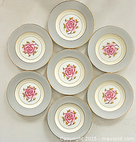 Seven Coalport porcelain plates arranged in a circular pattern showing the consistent rose design and gold-edged borders.