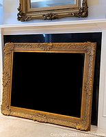 Front view of the large gilt wood frame leaning against hearth, showing overall look and design.