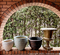 Group photo of four planters including beige, blue, dark brown ceramic and tall gold urn on brick surface with greenery background